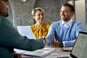 Free photo happy couple shaking hands with real estate agent after successful agreement in the office