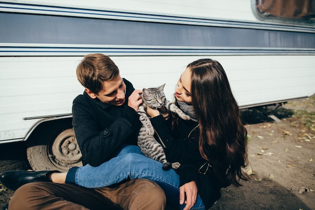 무료 사진 행복한 커플은 회색 고양이와 함께 바닥에 앉아있다. 고양이와 놀고 사랑에 아름 다운 커플입니다.