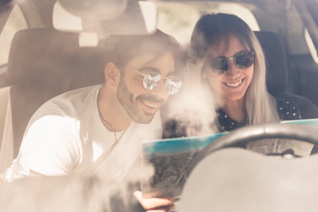 Happy couple sitting in car looking at map