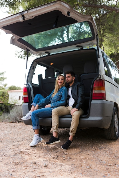 Coppie felici che si siedono sul tronco di automobile