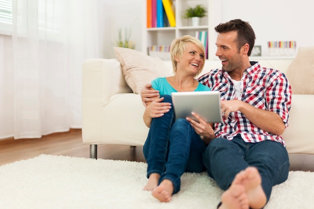 Happy couple sitting on carpet at home and using digital tablet
