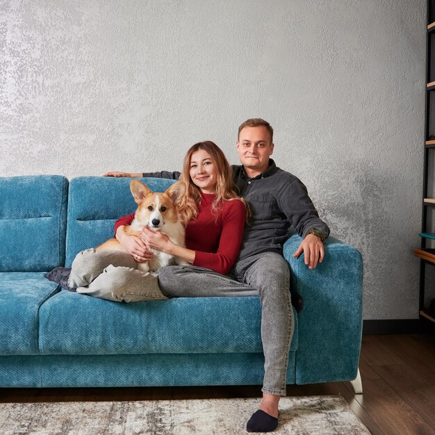 Счастливая пара сидит на диване с очаровательной собакой корги