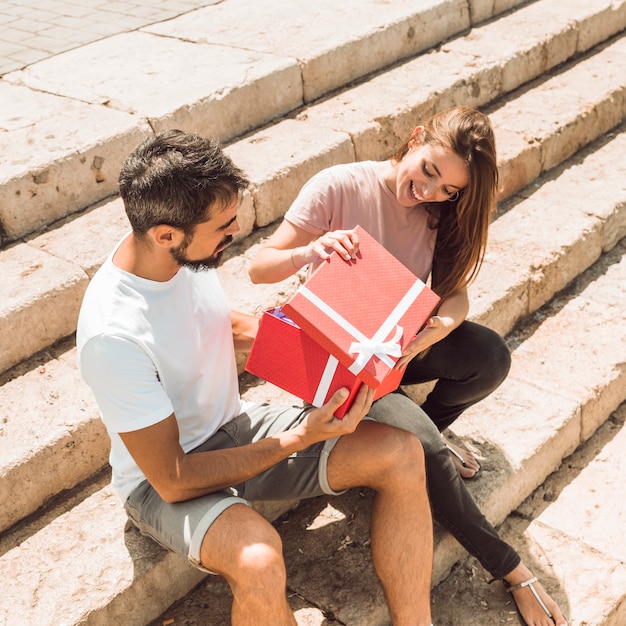 Happy couple sitting on staircase opening red gift box