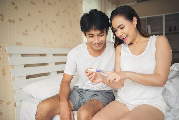 寝室で肯定的な妊娠検査を見つけた後に笑う幸せなカップル