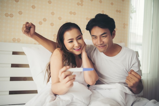 Happy couple smiling after find out positive pregnancy test in bedroom 