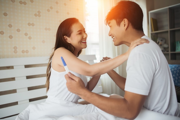 침실에서 긍정적 인 임신 테스트를 찾은 후 웃고 행복한 커플