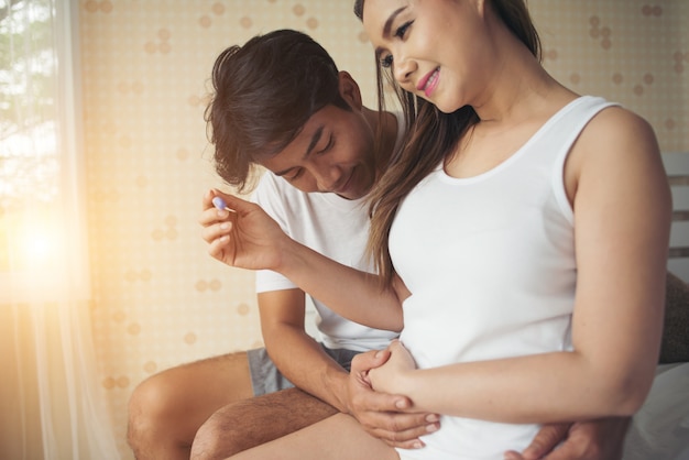 Happy couple smiling after find out positive pregnancy test in bedroom 