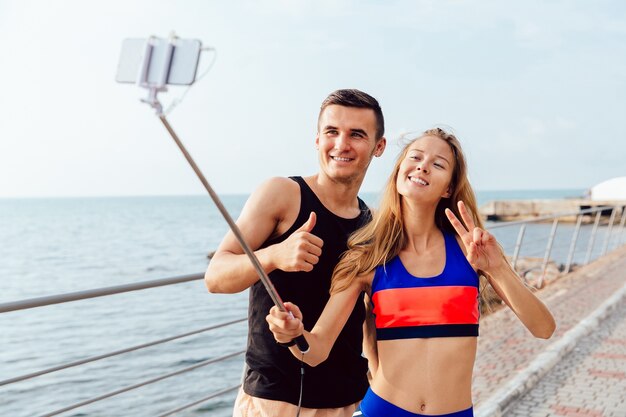 Happy couple in sportswear showing a thumb up and peace sign while taking a selfie