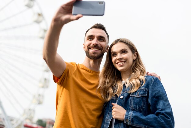 Happy couple taking a self photo in front of ferris wheel