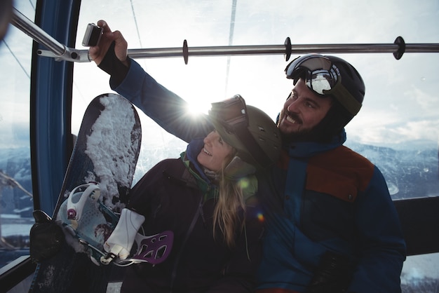 Happy couple taking selfie in overhead cable car against sky