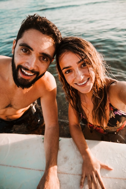 Free photo happy couple taking selfie in sea with surfboard