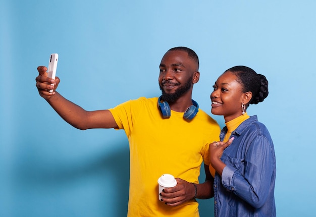 스튜디오에서 스마트폰으로 셀카를 찍고 함께 추억을 만드는 행복한 커플. 현대 남자 친구와 여자 친구는 휴대 전화로 사진을 찍고 배경 위에 기술을 수용하고 사용합니다.