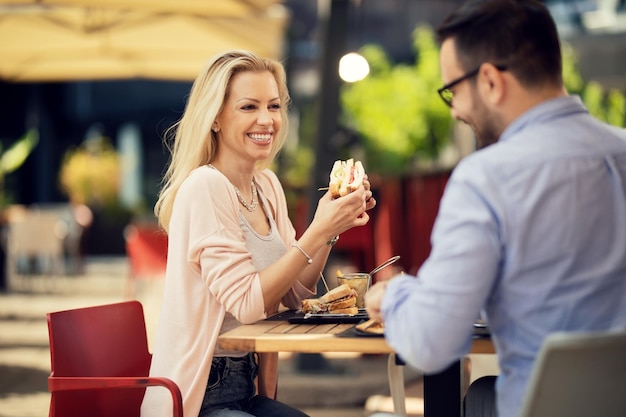 Coppia felice parlando tra loro durante l'ora di pranzo in un ristorante focus è sulla donna che mangia un panino