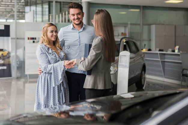 Счастливая пара разговаривает с агентом автосалона