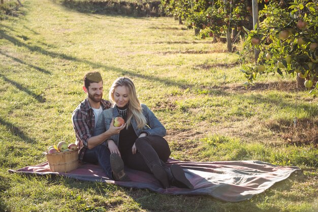 Happy couple together sitting on a blanket in apple orchard