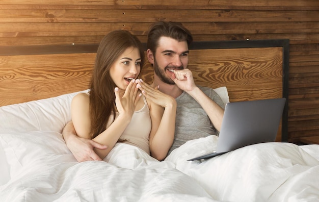 Happy couple using laptop in bed at bedroom