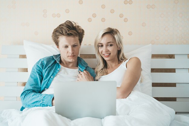 Счастливая пара, используя портативный компьютер на кровати