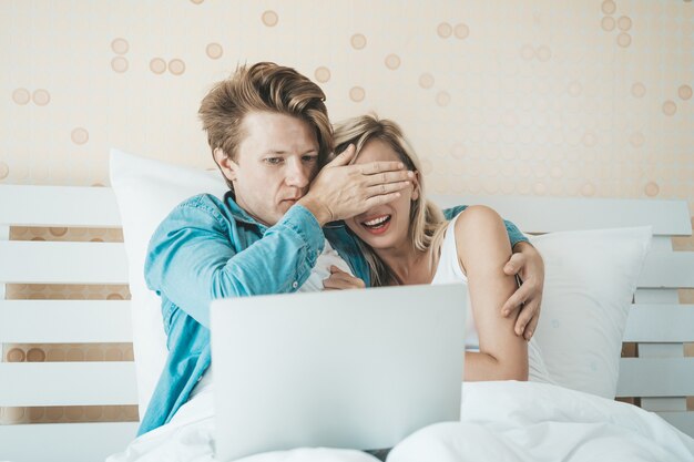 Счастливая пара, используя портативный компьютер на кровати
