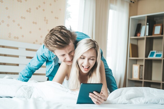 Счастливая пара с помощью планшетного компьютера на кровати