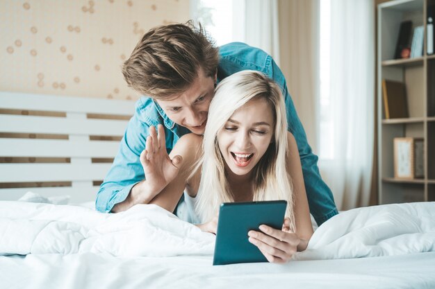 침대에서 태블릿 컴퓨터를 사용하여 행복한 커플