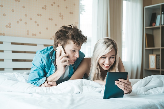 幸せなカップルはベッドの上にタブレットコンピューターを使用して