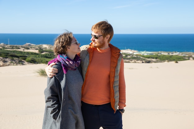 Free photo happy couple in warm clothes hugging and walking on sand, spending leisure time at sea