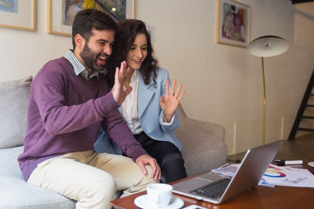 Free photo happy couple waving hello at computer screen