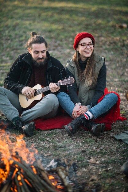 Happy couple with guitar near campfire