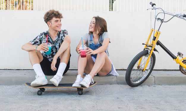 Счастливая пара с скейтбордом пить сок рядом с велосипедом