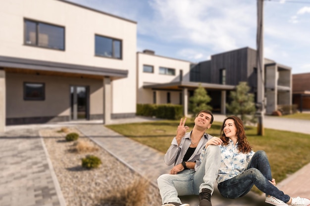 Happy couple with their new house at the background and smiling.