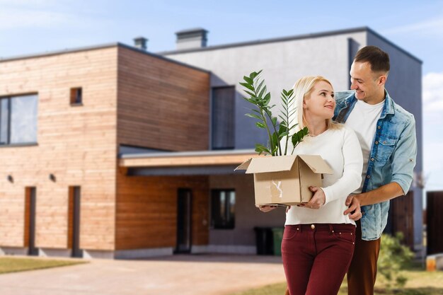 Happy couple with their new house at the background and smiling.