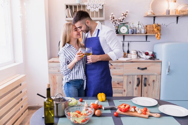 Happy couple with wine glasses hugging in kitchen