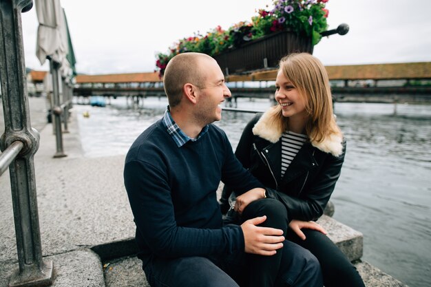 Happy couple. Young couple in love sits on pier looking at each other and smiling.