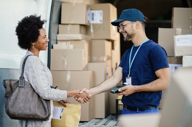 Free photo happy courier handshaking with african american woman while delivering her a package