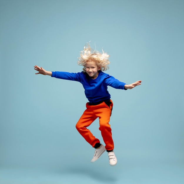 파란색 스튜디오 배경에 격리된 행복한 곱슬머리 소년은 행복하고 쾌활한 성실한 Copyspace 어린 시절 교육 감정 개념을 보입니다.
