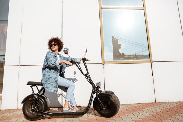 Happy curly woman sitting on a modern motorbike