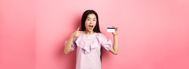 Happy cute asian woman showing plastic credit card recommending bank special deal standing against p