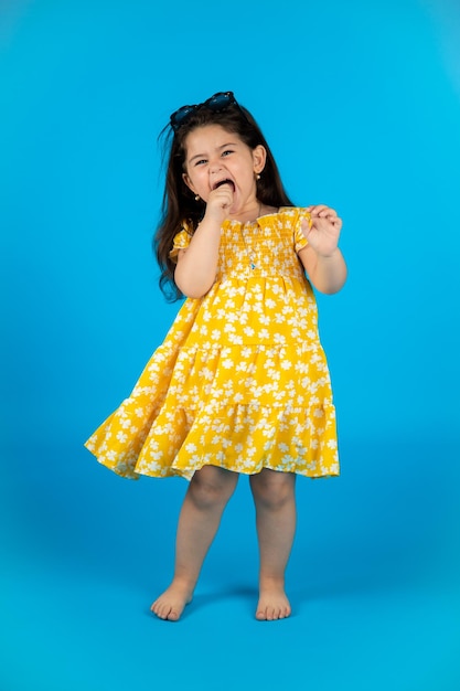 Happy cute baby girl fashionable yellow baby clothes posing studio on blue background