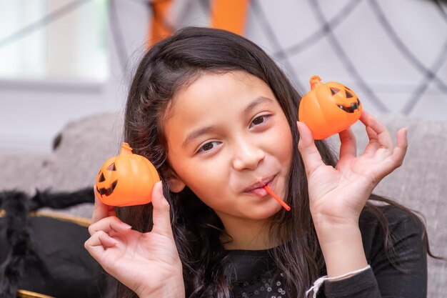 Happy cute boy girl in costume during Halloween party holding pumpkin Jacko'lantern beside her eyes