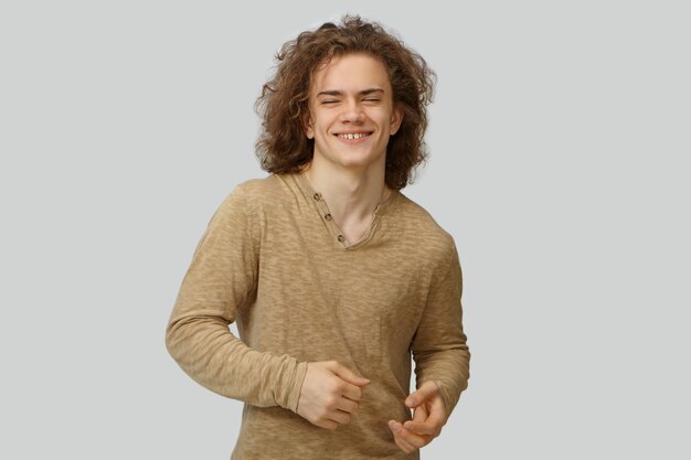 Happy cute guy in stylish long sleeved shirt having fun, laughing at joke, moving hands as if dancing. Funny friendly looking young Caucasian man smiling broadly, showing white straight teeth