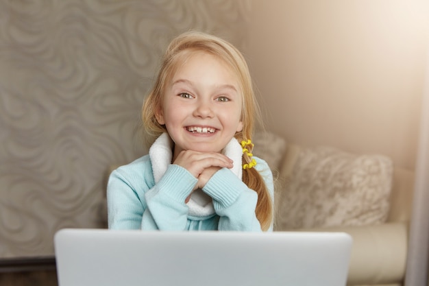 Free photo happy cute little girl with messy ponytail smiling happily, resting face on hands