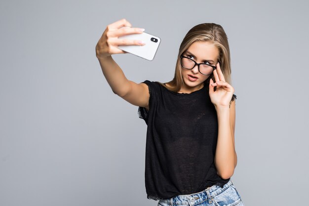 회색 배경 위에 휴대 전화에서 selfie를 만드는 행복 한 귀여운 여자.