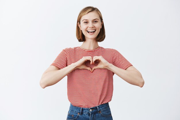 Happy cute young woman showing love gesture, making heart with fingers