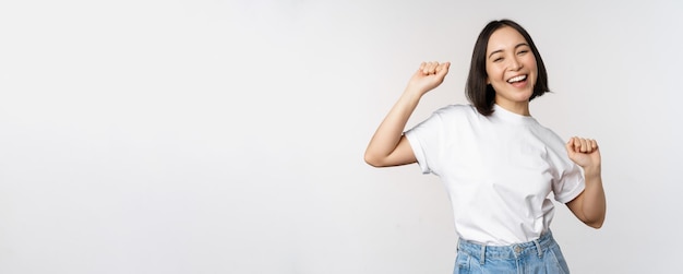 Free photo happy dancing korean girl posing against white background wearing tshirt