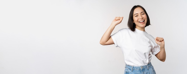 無料Photo tシャツを着て白い背景に対してポーズをとって幸せなダンス韓国の女の子