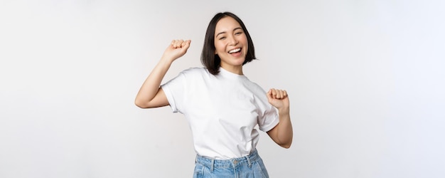 Free photo happy dancing korean girl posing against white background wearing tshirt