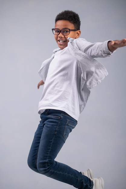 Happy dark-haired bespectacled young boy jumping up