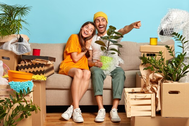 Happy dark haired girl leans at shoulder of boyfriend who holds wrapped potted domestic plant