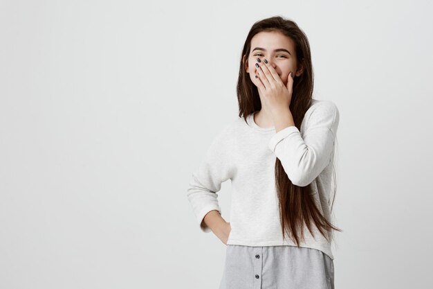 Happy dark-haired woman closing mouth with hand