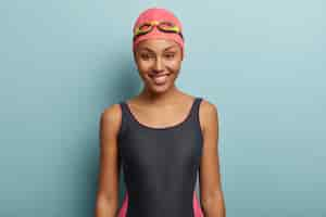 Free photo happy dark skinned female going to swim, wears pink swimcap and goggles